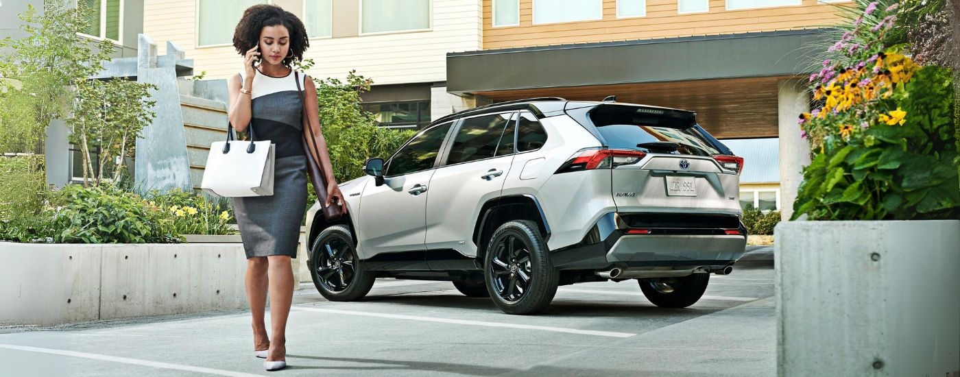 A woman walking away from a silver and black 2020 Toyota RAV4 Hybrid.