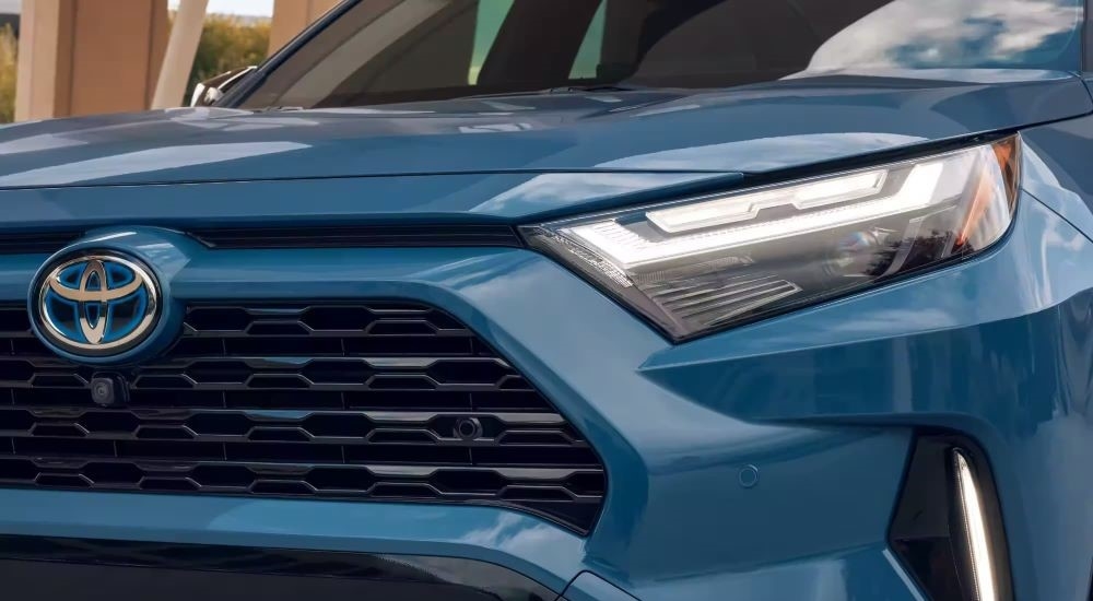 A close up shows the driver side headlight on a blue 2023 Toyota RAV4.