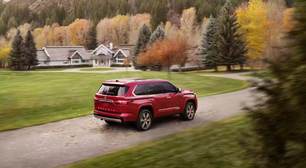 A red 2023 Toyota Sequoia is shown driving on a road near a house.