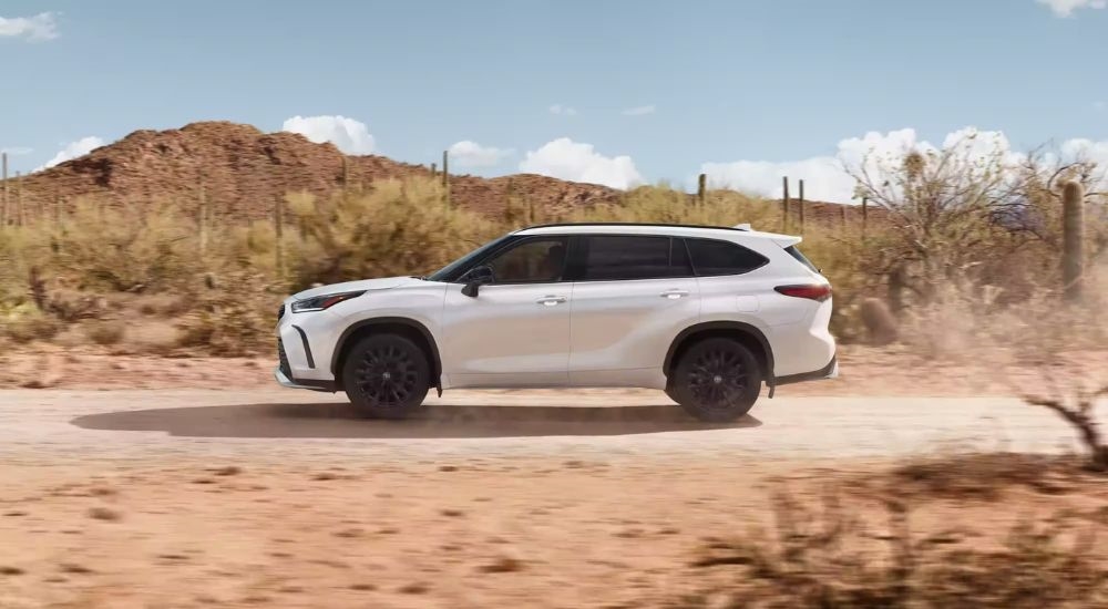 Side view of a white 2024 Toyota Highlander XSE driving through on a dusty trail.