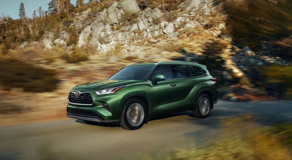 A green 2024 Toyota Highlander Platinum driving past a rocky hillside.