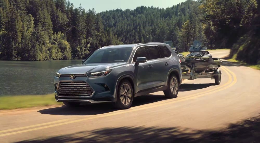 A grey 2024 Toyota Grand Highlander Platinum Hybrid MAX towing jet skis past a body of water.