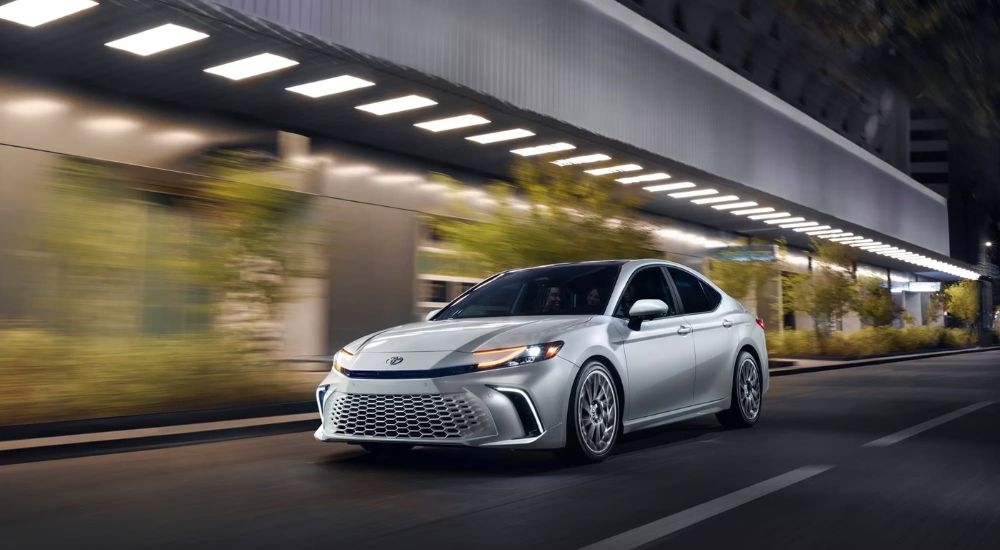 A silver 2025 Toyota Camry XSE driving on a city street at night.