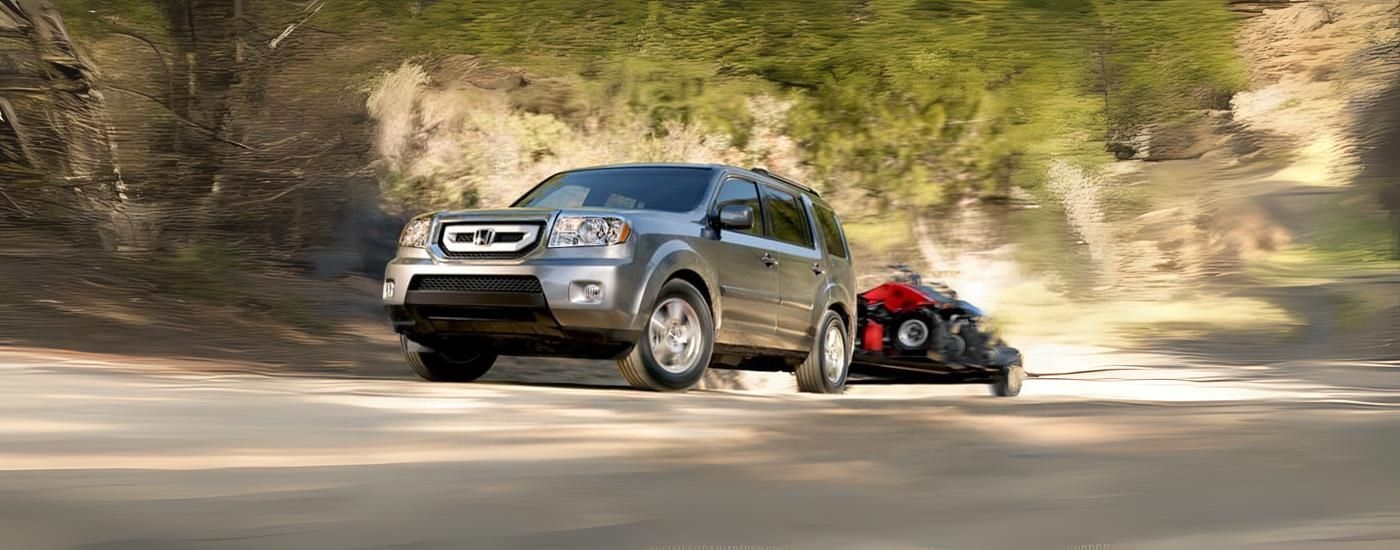 A silver 2011 Honda Pilot is shown towing ATVs.