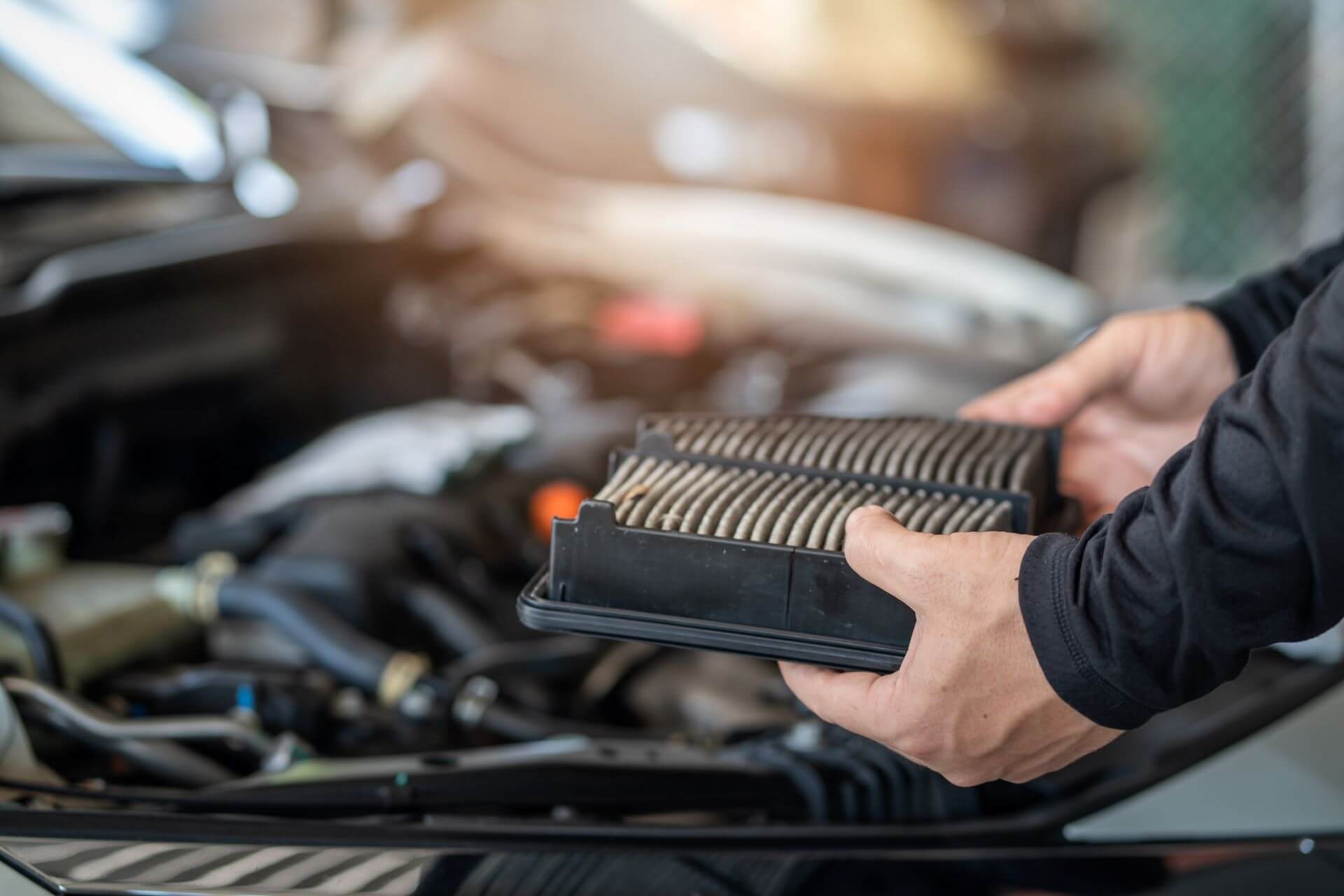 Service technician holding dirty air filter in hands with engine in background.