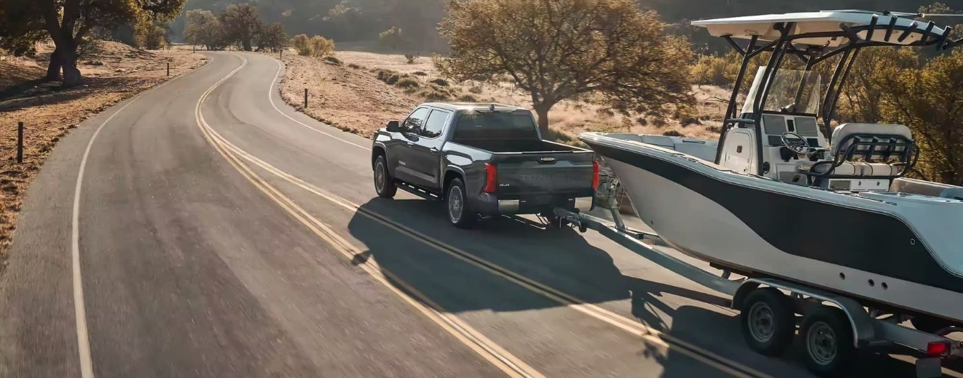 A grey 2023 Toyota Tundra for sale is shown towing a boat on a winding road.