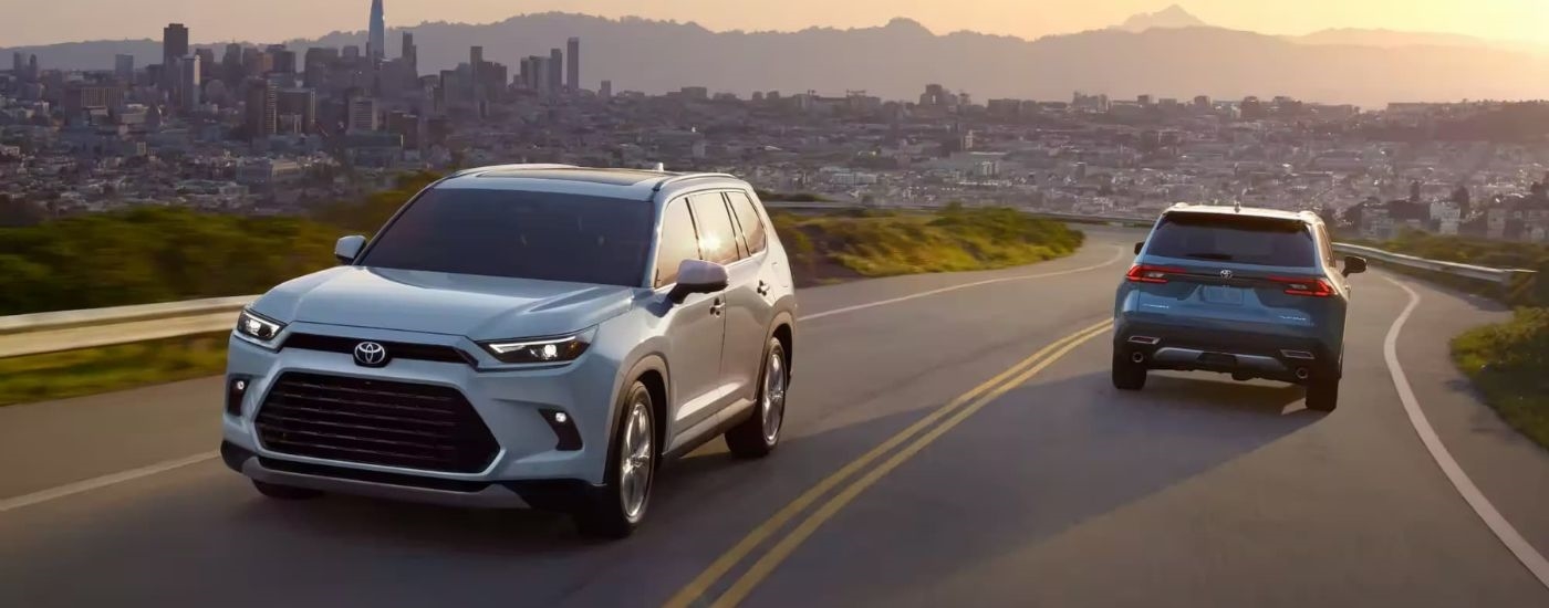 A silver 2024 Toyota Grand Highlander is shown driving near a city.