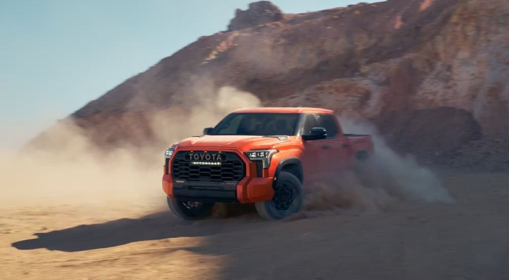 An orange 2024 Toyota Tundra TRD Pro is shown kicking up dust off-road.