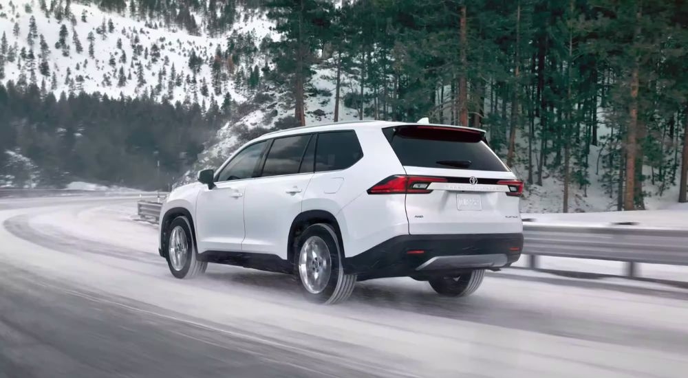 A white 2024 Toyota Grand Highlander is shown rounding a snowy corner.