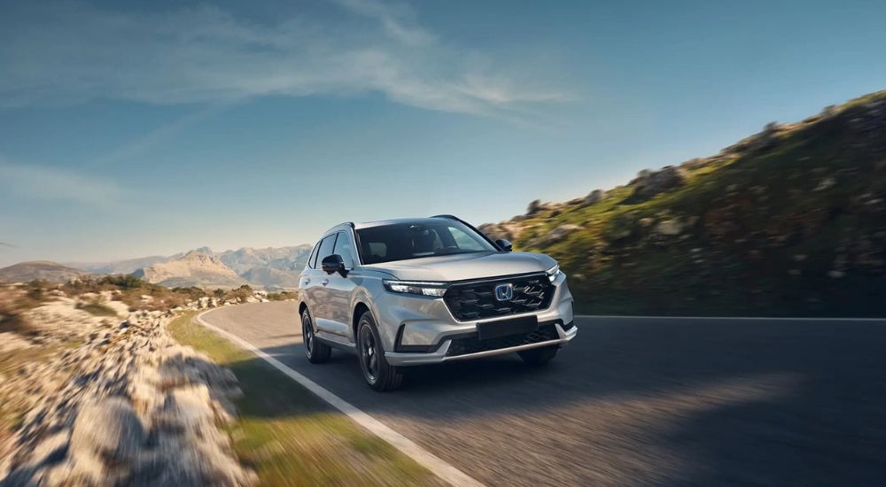 A white 2025 Honda CR-V Hybrid is shown on an open road after looking at SUVs for sale.