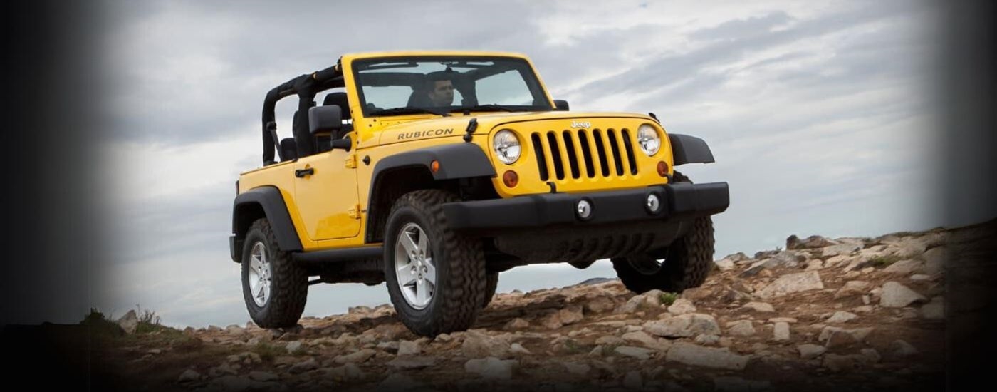 A yellow 2011 Jeep Wrangler Rubicon is shown on a cloudy day.