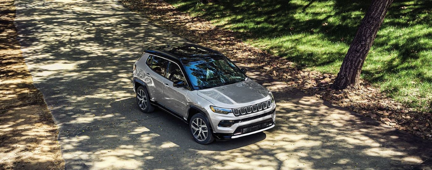 A silver 2025 Jeep Compass is shown on a path after leaving a Jeep dealership.