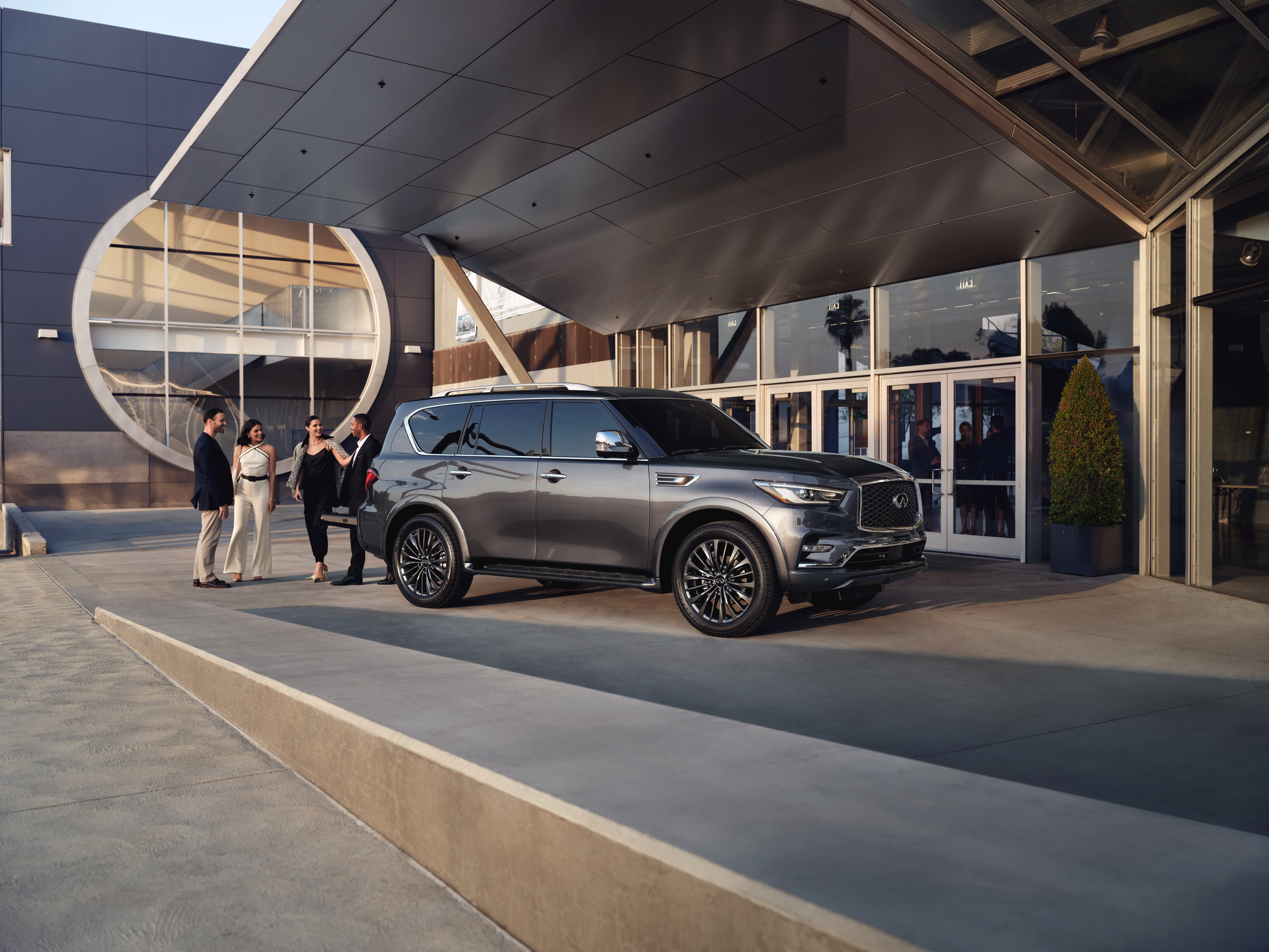  The 2023 Infiniti QX80 parked outside a modern building in Denver with a group of people chatting nearby.