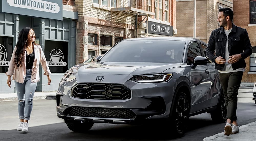 A pair of people walk away from a grey 2025 Honda HR-V parked beside a curb.