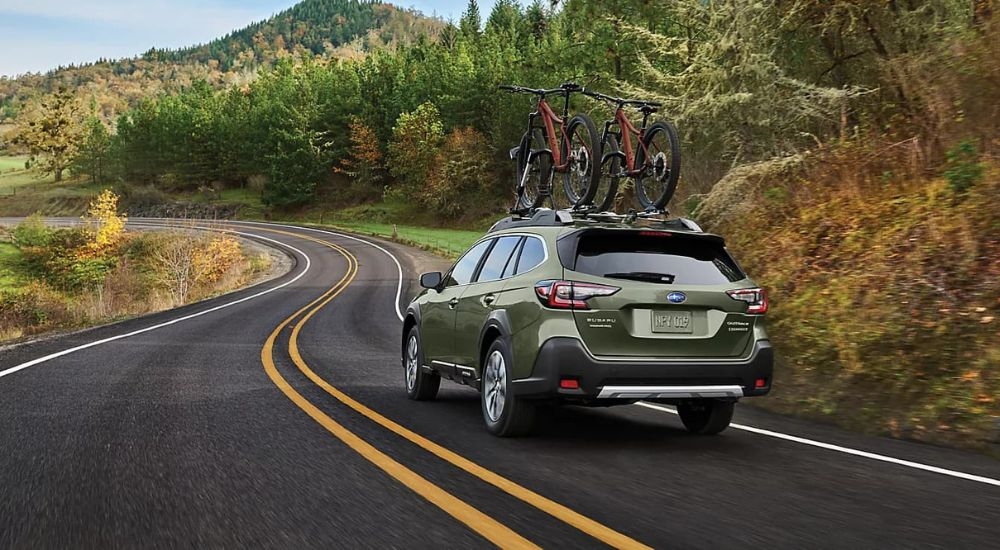 A green 2024 Subaru Outback driving down a winding road.