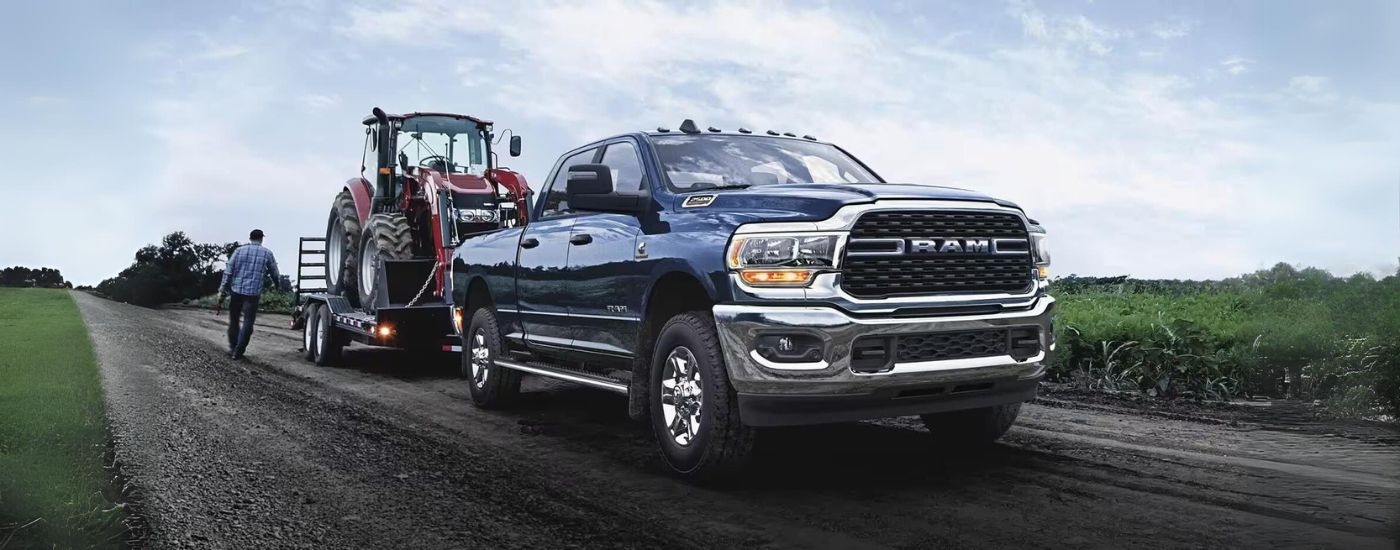 A blue 2023 Ram 2500 is shown towing a red tractor.