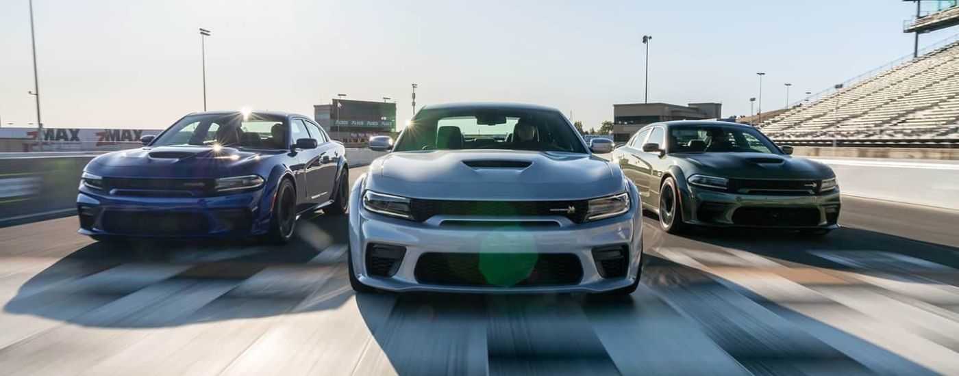 A blue, a silver, and a green 2020 Dodge Charger are shown racing on a race track.