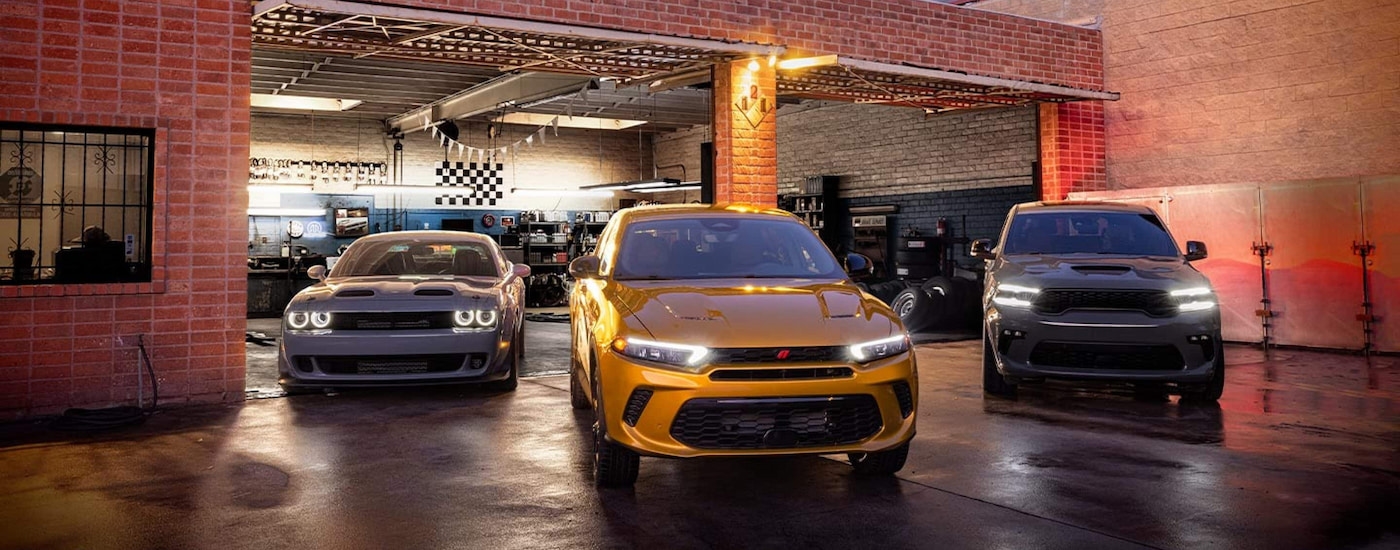 A grey 2024 Dodge Challenger SRT Super Stock, a yellow Hornet GT, and a grey Durango SRT parked in front of a garage.