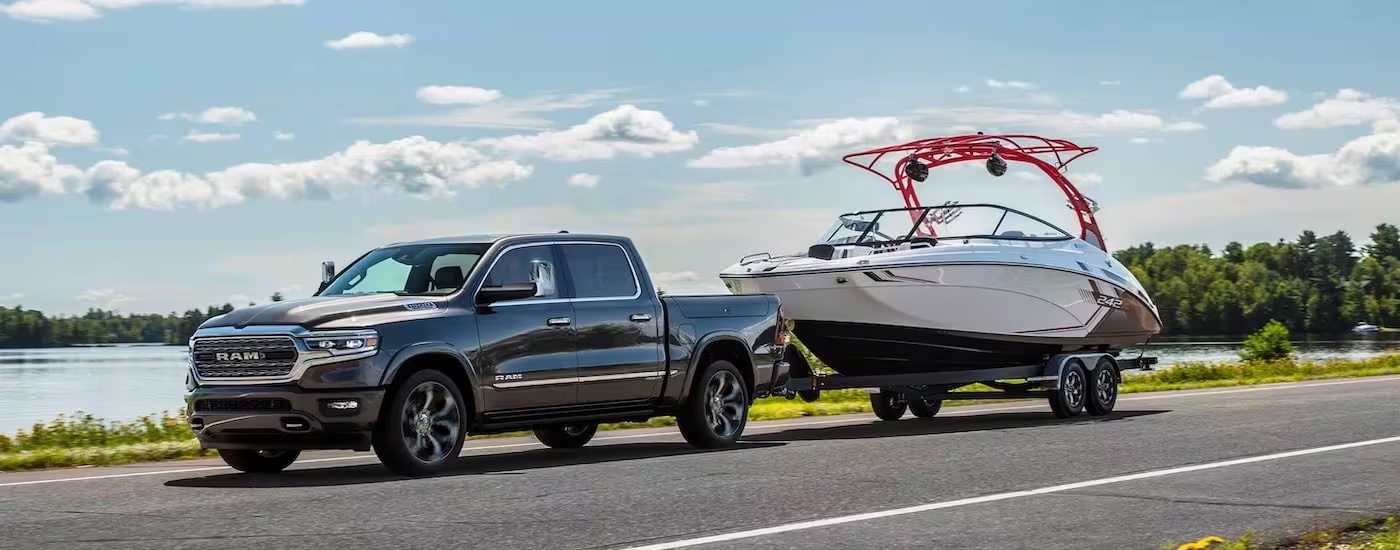 A grey 2024 Ram 1500 for sale is shown from the side while towing a boat.
