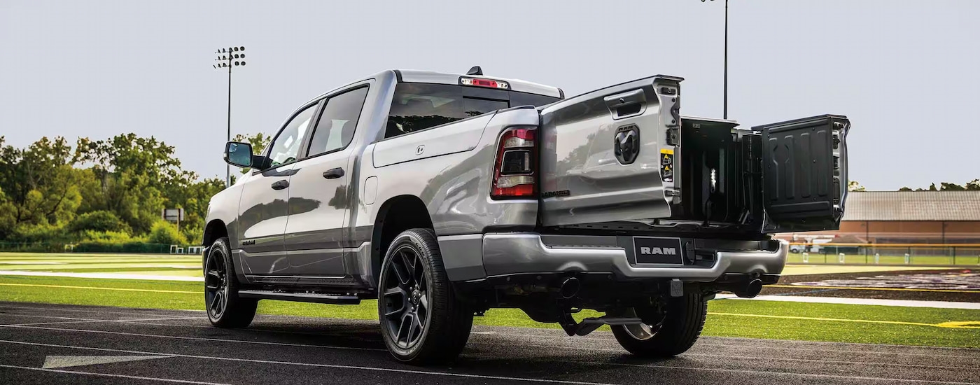 A silver 2024 Ram 1500 is shown from the rear at an angle with the tailgate open.
