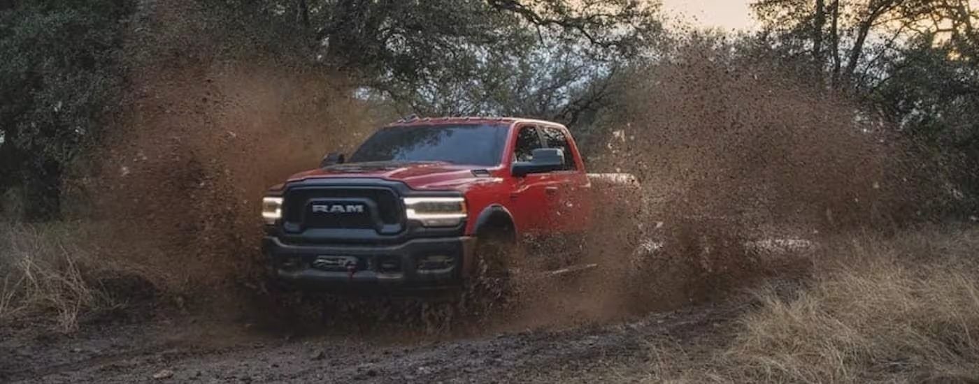 A red 2022 Ram 2500 HD Power Wagon is shown from the front while driving through mud after leaving a dealership with Ram trucks for sale.