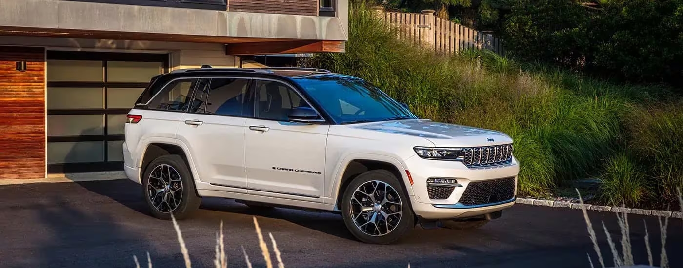 A white 2023 Jeep Grand Cherokee is shown from the side in a driveway.