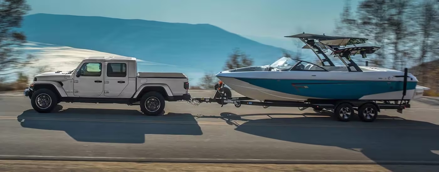 A silver 2024 Jeep Gladiator is shown from the side while towing a boat after leaving a Jeep dealer near Red Hook.