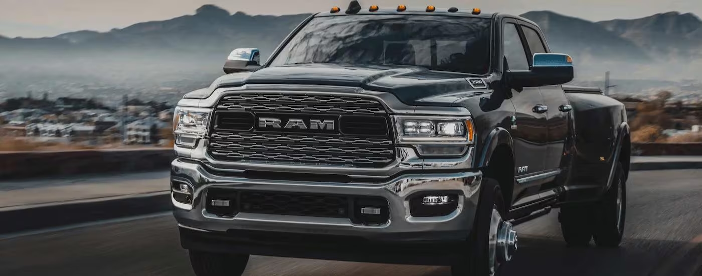 A black 2023 Ram 3500 is shown driving on an open road away from a town.