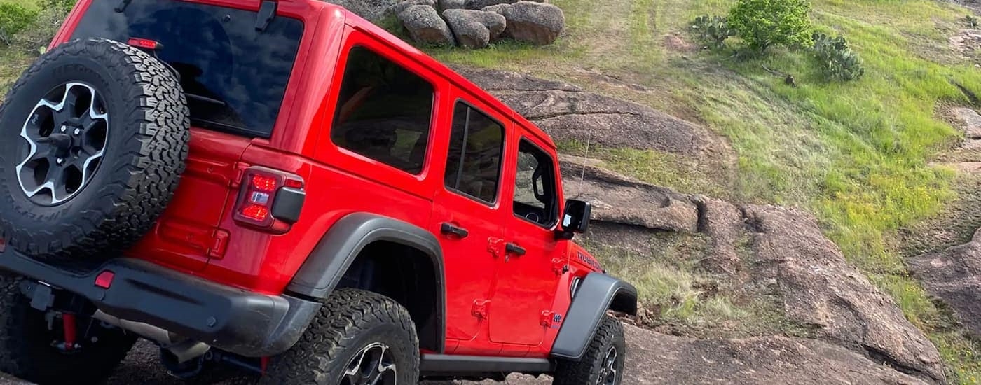 A 2023 Jeep Wrangler Rubicon is shown from the rear off-roading on a steep rocks.