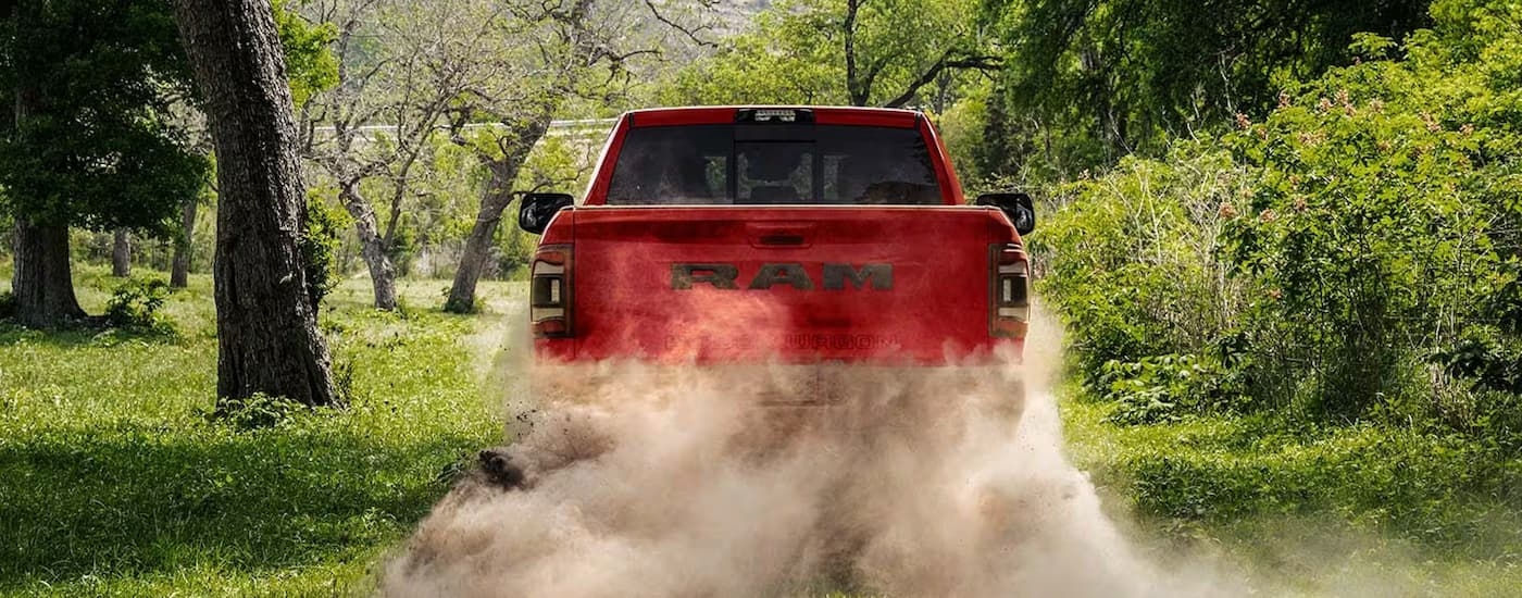 A red 2023 Ram 2500 Power Wagon is shown from the rear driving on a dusty road.