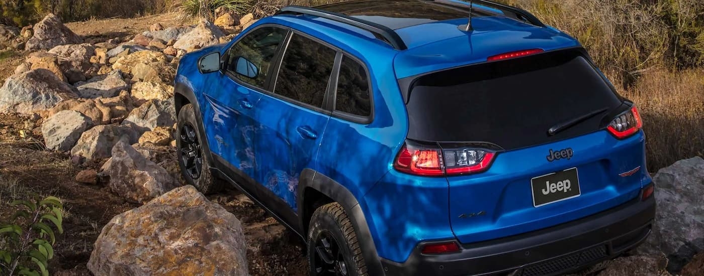 A blue 2022 Jeep Cherokee Trailhawk is shown from the rear off-roading on a rocky trail.