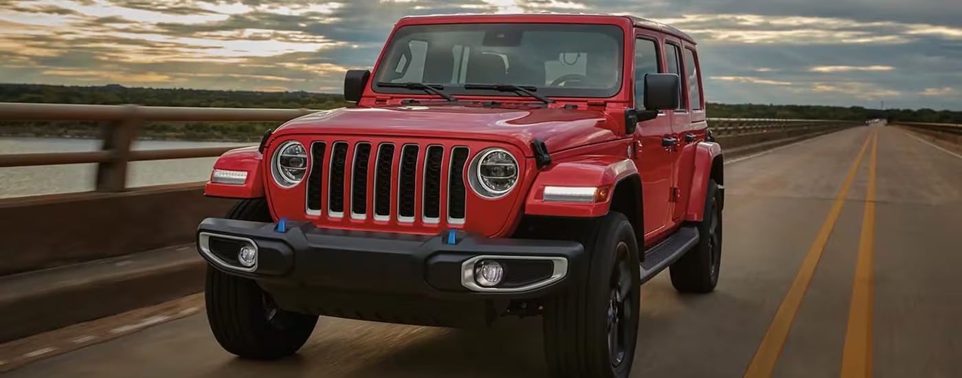 A red 2023 Jeep Wrangler is shown driving on a bridge.