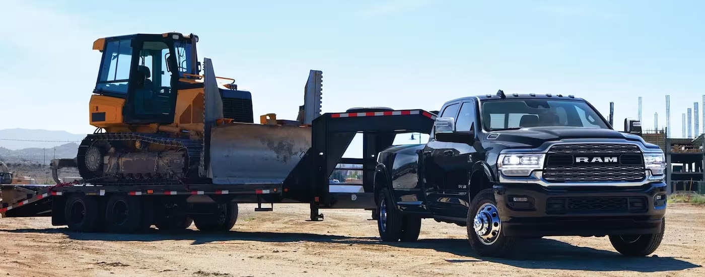 A black 2024 Ram 3500 is shown from the front at an angle while towing a bulldozer.