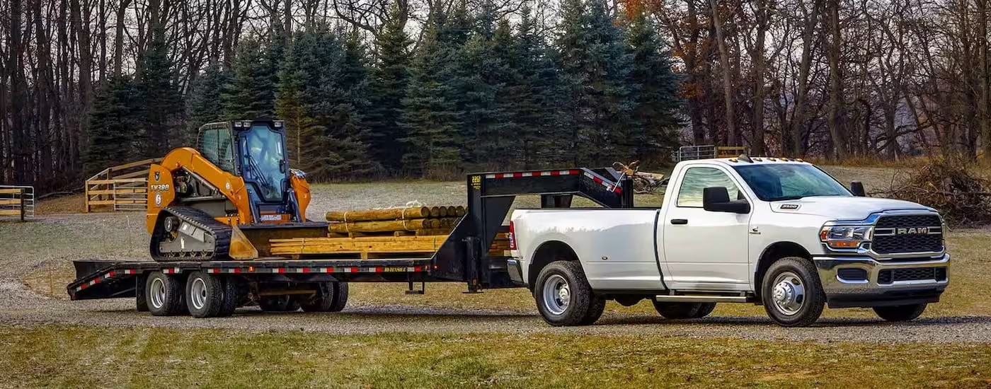 A white 2024 Ram 3500 is shown while towing a skid-steer.