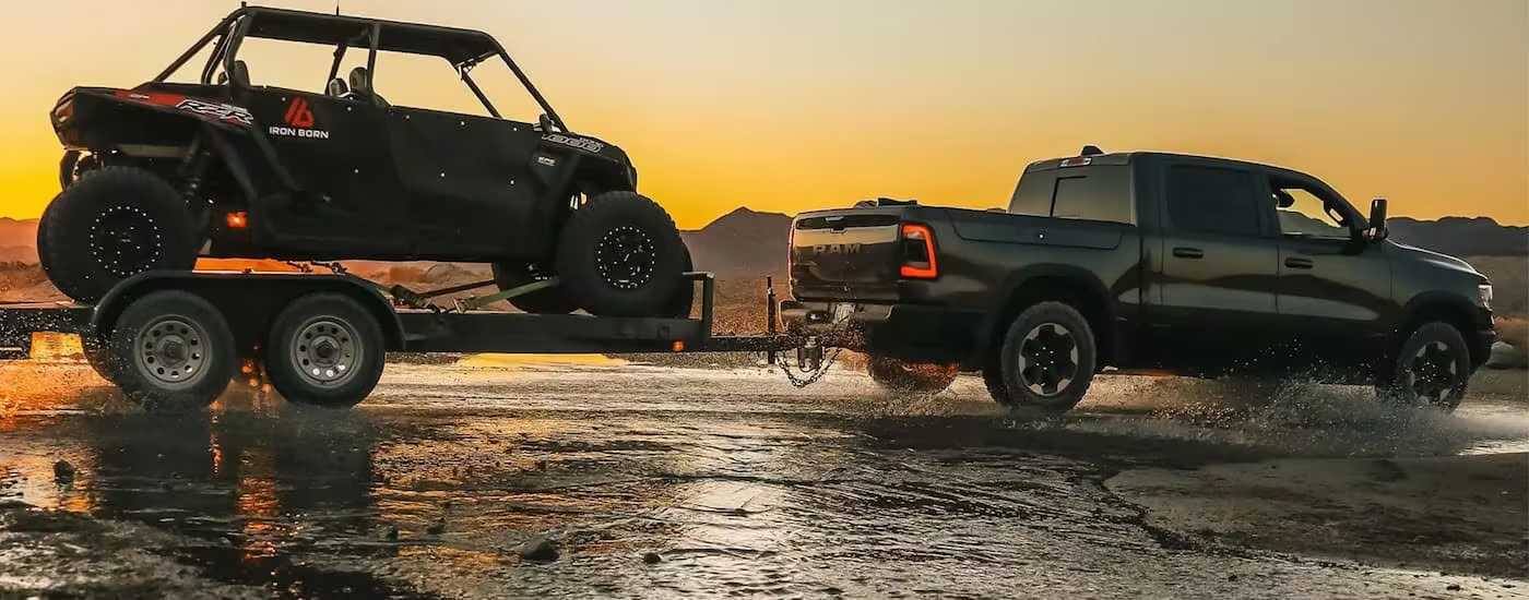 A black 2022 Ram 1500 is shown towing an UTV on a trailer.