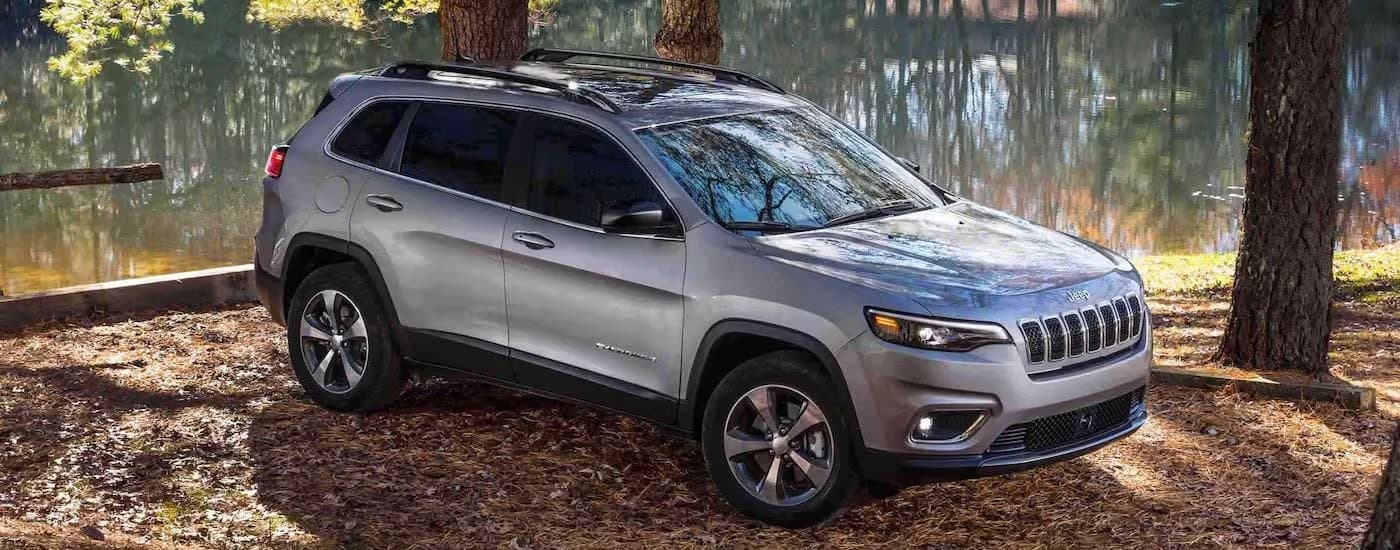 A silver 2022 Jeep Cherokee, a popular Jeep for sale near you, is shown parked near a small pond.