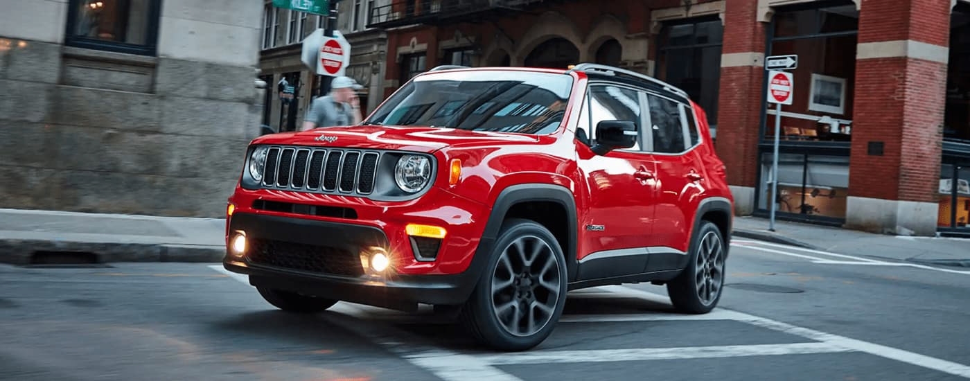 A red 2023 Jeep Renegade is shown driving on a city street.