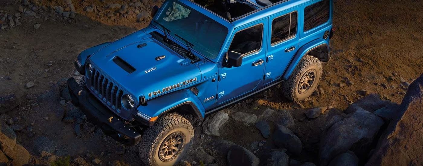 A blue 2023 Jeep Wrangler Rubicon is shown parked on a rocky dirt trail.