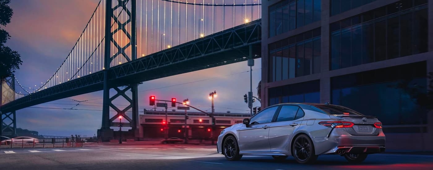 A rear view of a white 2020 Toyota Camry driving under a bridge.