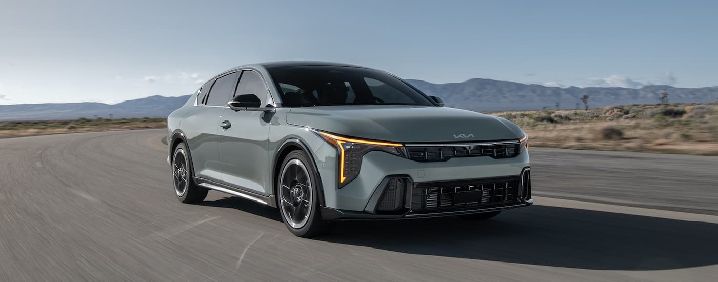 A green 2025 Kia K4 for sale is driving on an open road.