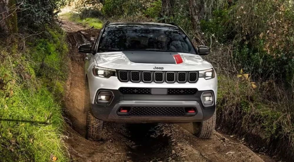 A white 2024 Jeep Compass Trailhawk is shown off-roading after leaving a Jeep dealership.