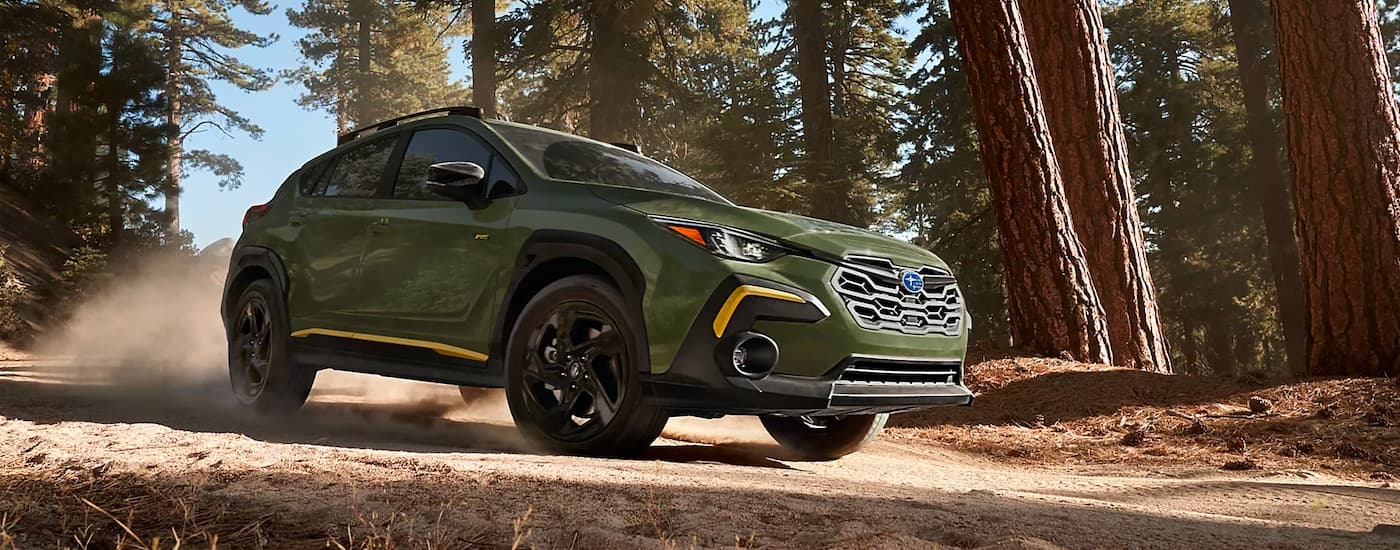 A green 2024 Subaru Crosstrek Sport driving in a forest.