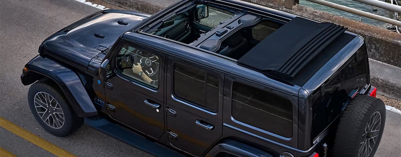 A black 2024 Jeep Wrangler driving with the roof open.