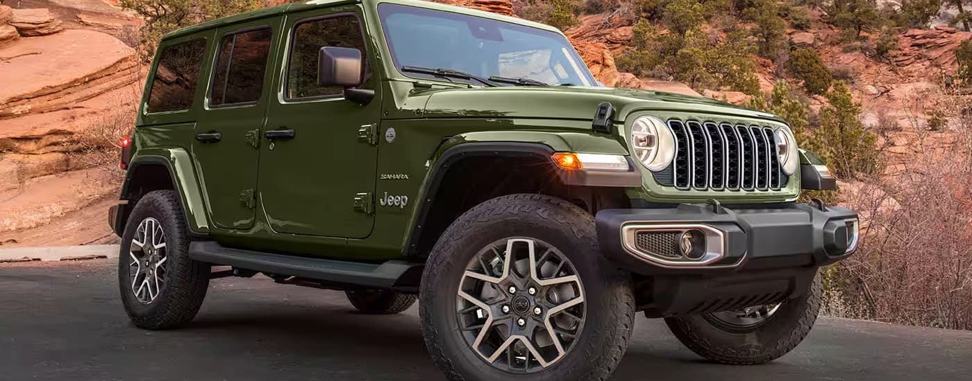 A green 2024 Jeep Wrangler is parked near a set of rocks.