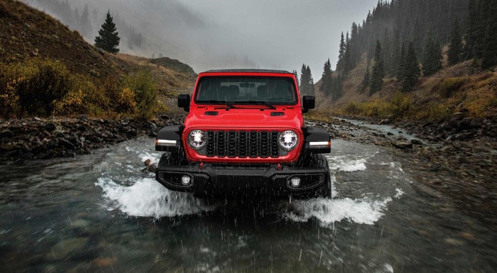 A red 2024 Jeep Wrangler is shown driving through a river after leaving a Jeep dealer near Kingston