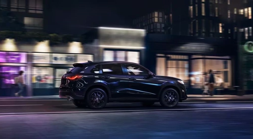 Side view of a black 2024 Honda HR-V Sport driving through a city at night after visiting a Honda dealer near Mahwah.