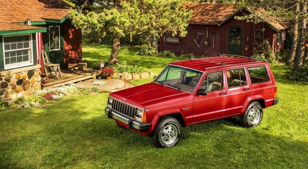 A red 1984 Jeep Cherokee is shown parked on a grassy lawn.