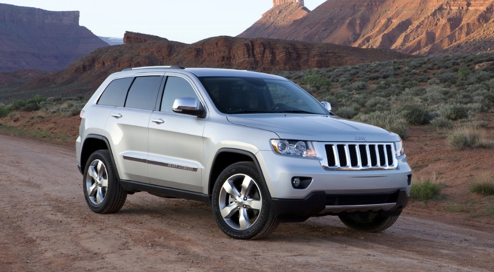 A silver 2011 Jeep Grand Cherokee is shown on a dirt road after leaving a used Jeep dealership.