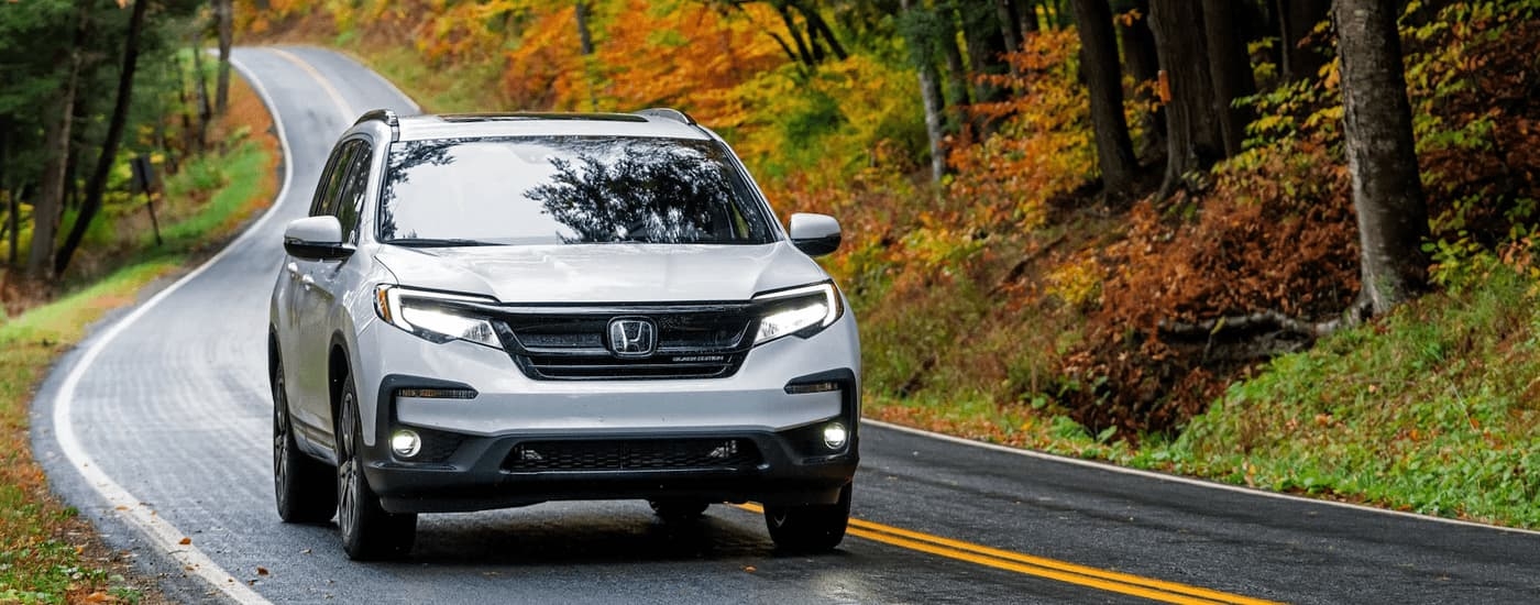 A white 2022 Honda Pilot Black Edition driving on a rural road.