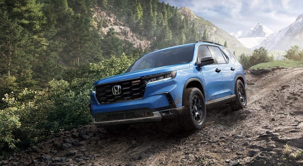 A blue 2024 Honda Pilot TrailSport off-roading down a rocky hill.